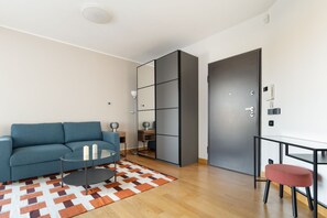 Ein modernes Wohnzimmer mit einer Couch, einem Glastisch, einem gemusterten Teppich, einer verspiegelten Trennwand und einer Tür.