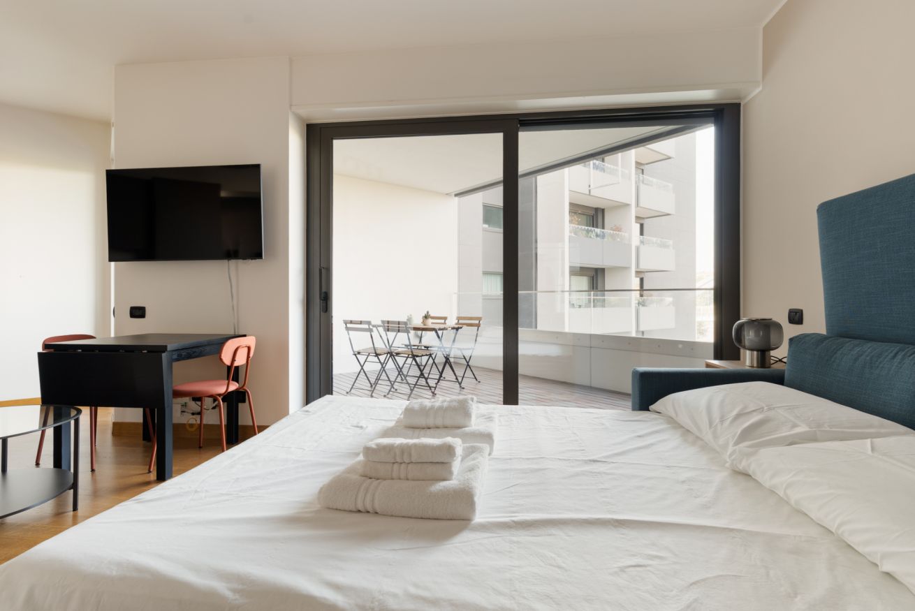Ein Hotelzimmer mit Bett, Schreibtisch, Sessel, Fernseher und einem Balkon mit Tisch und Stühlen.