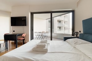 Ein Hotelzimmer mit Bett, Schreibtisch, Sessel, Fernseher und einem Balkon mit Tisch und Stühlen.