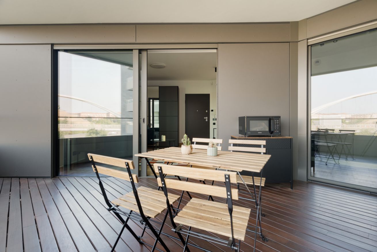 Ein moderner Balkon mit Holztisch und -stühlen, einer Mikrowelle und Blick auf die Stadtlandschaft.