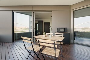 Ein moderner Balkon mit Holztisch und -stühlen, einer Mikrowelle und Blick auf die Stadtlandschaft.