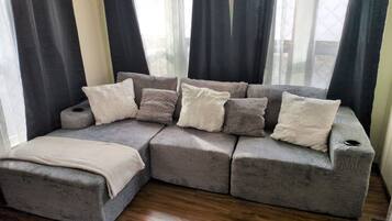 Ein modulares Sofa mit vielen Kissen in einem Raum mit Holzboden und großen, mit Vorhängen versehenen Fenstern.
