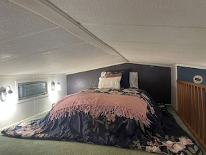 Ein Schlafzimmer mit einem Bett, einem Fenster mit Jalousien, einer Wandleuchte und einer Holzverkleidung an der Wand.