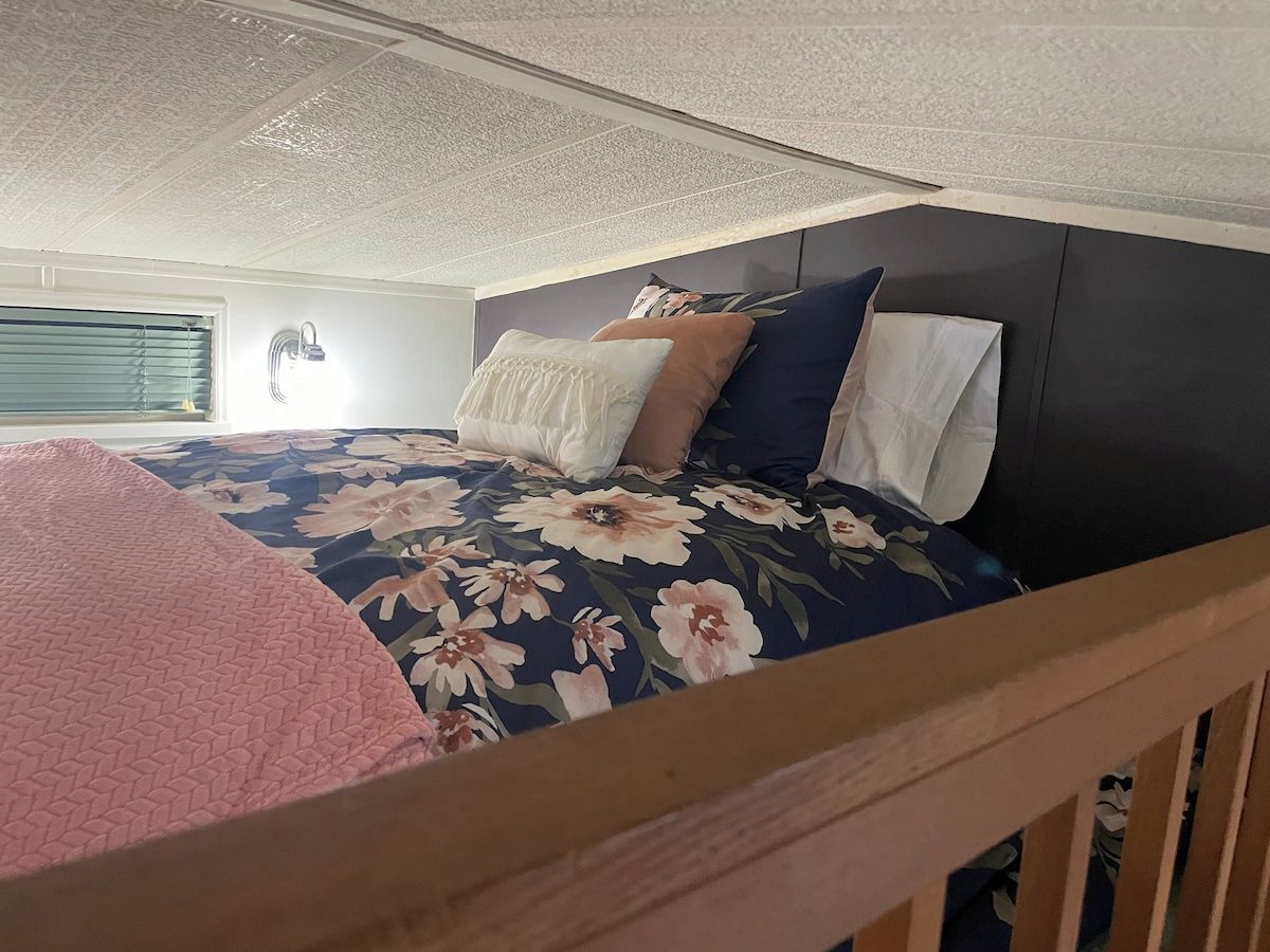 Ein Schlafzimmer mit einem Bett, Kissen, einem Kopfteil und einem Fenster mit Jalousien.