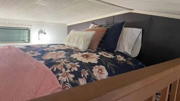 Ein Schlafzimmer mit einem Bett, Kissen, einem Kopfteil und einem Fenster mit Jalousien.