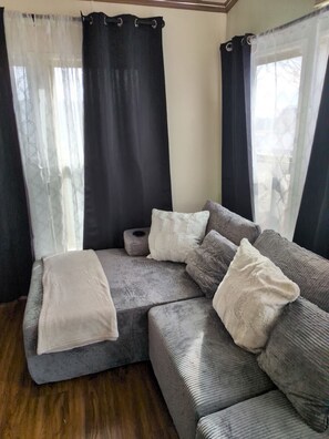 Eine Sitzecke mit einer Couch und Kissen, einem kleinen runden Tisch und einem Fenster mit Vorhängen.