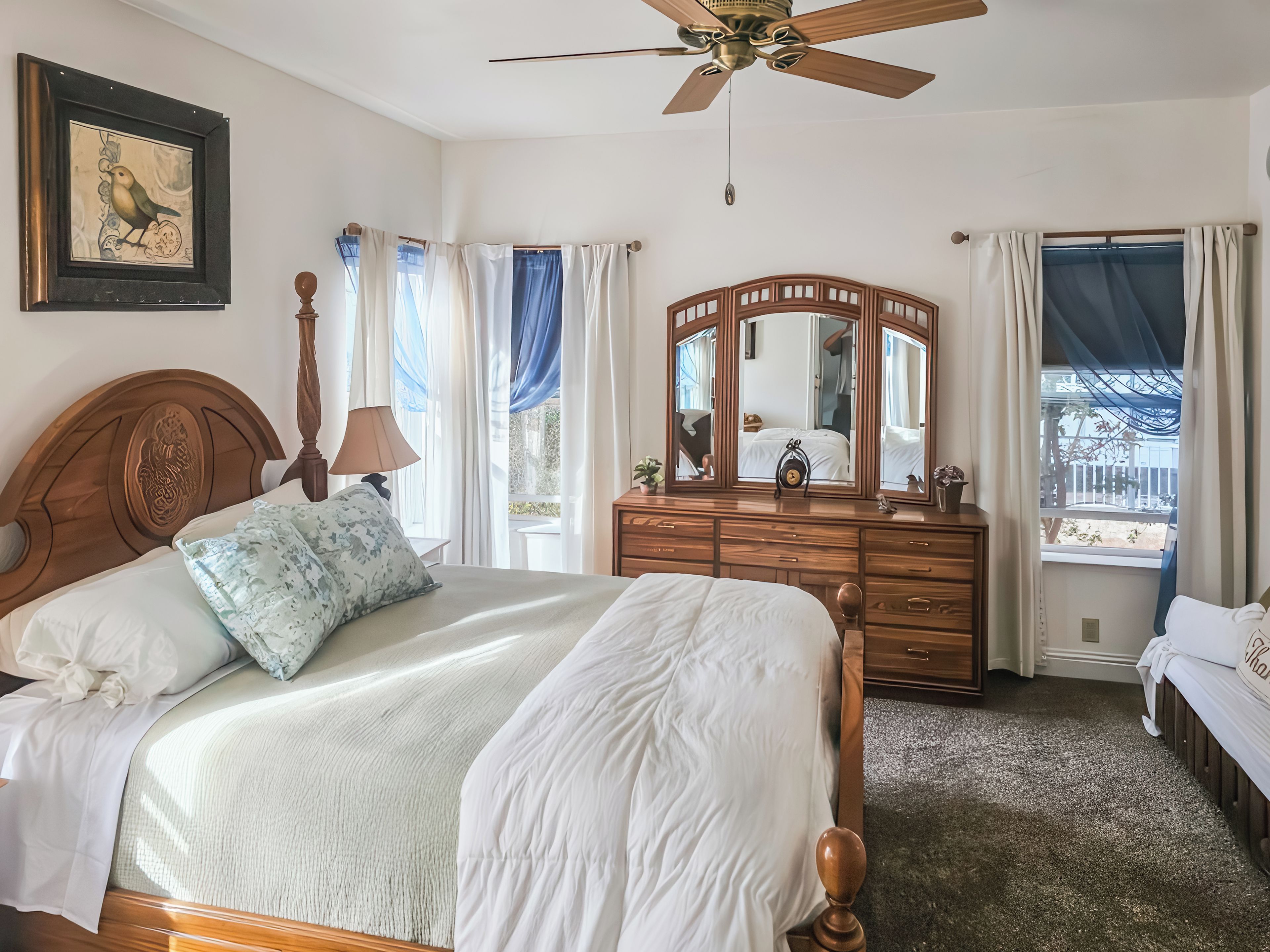 Een slaapkamer met een bed, een dressoir, een spiegel en een plafondventilator.