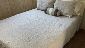 A bed with a textured white bedspread and two pillows, one striped and one plain, in a room with wooden paneling and a window. - Hickory Heaven by the Lake (New London)