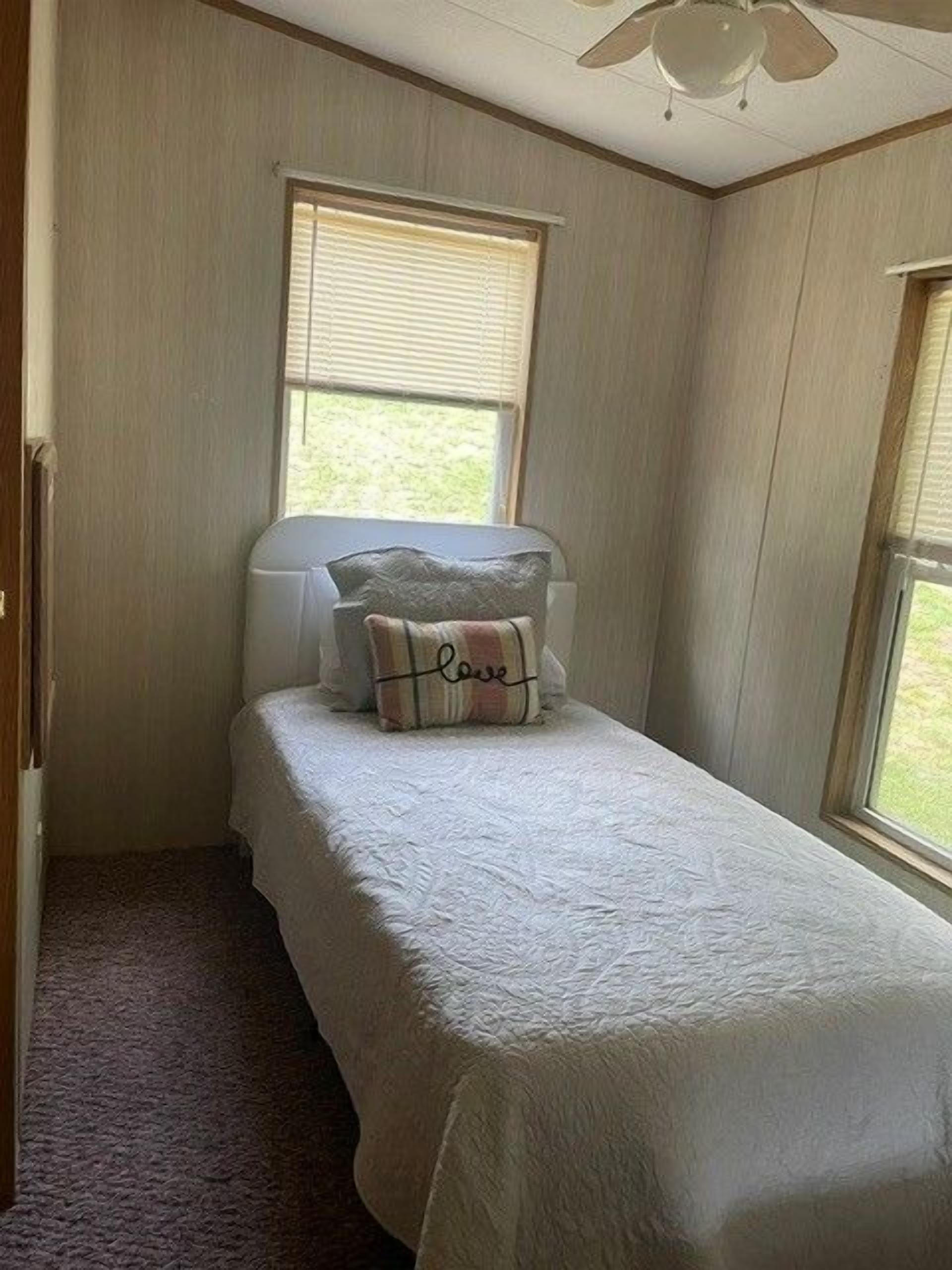 Un dormitorio pequeño con una cama individual, dos ventanas y un ventilador de techo.