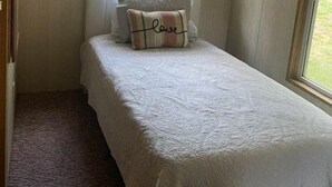 A small bedroom with a single bed, two windows, and a ceiling fan.
