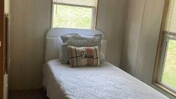 Un dormitorio pequeño con una cama individual, dos ventanas y un ventilador de techo.