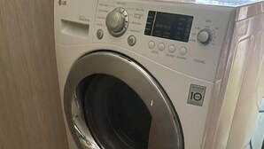 A front-loading washing machine in a laundry room with a tiled floor.
