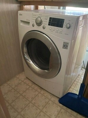 Une machine à laver à chargement frontal dans une buanderie dont le sol est carrelé.