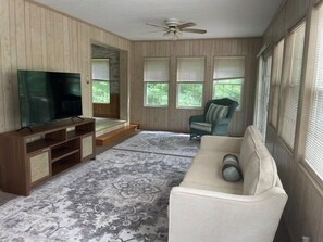 A living room with a flat-screen TV, a sofa, a chair, and a wooden entertainment unit.