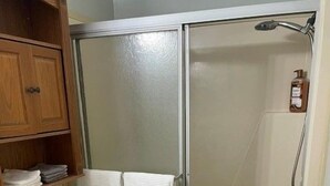 A bathroom with a toilet, a shower enclosure, and a wooden cabinet with toiletries. - Hickory Heaven by the Lake (New London)