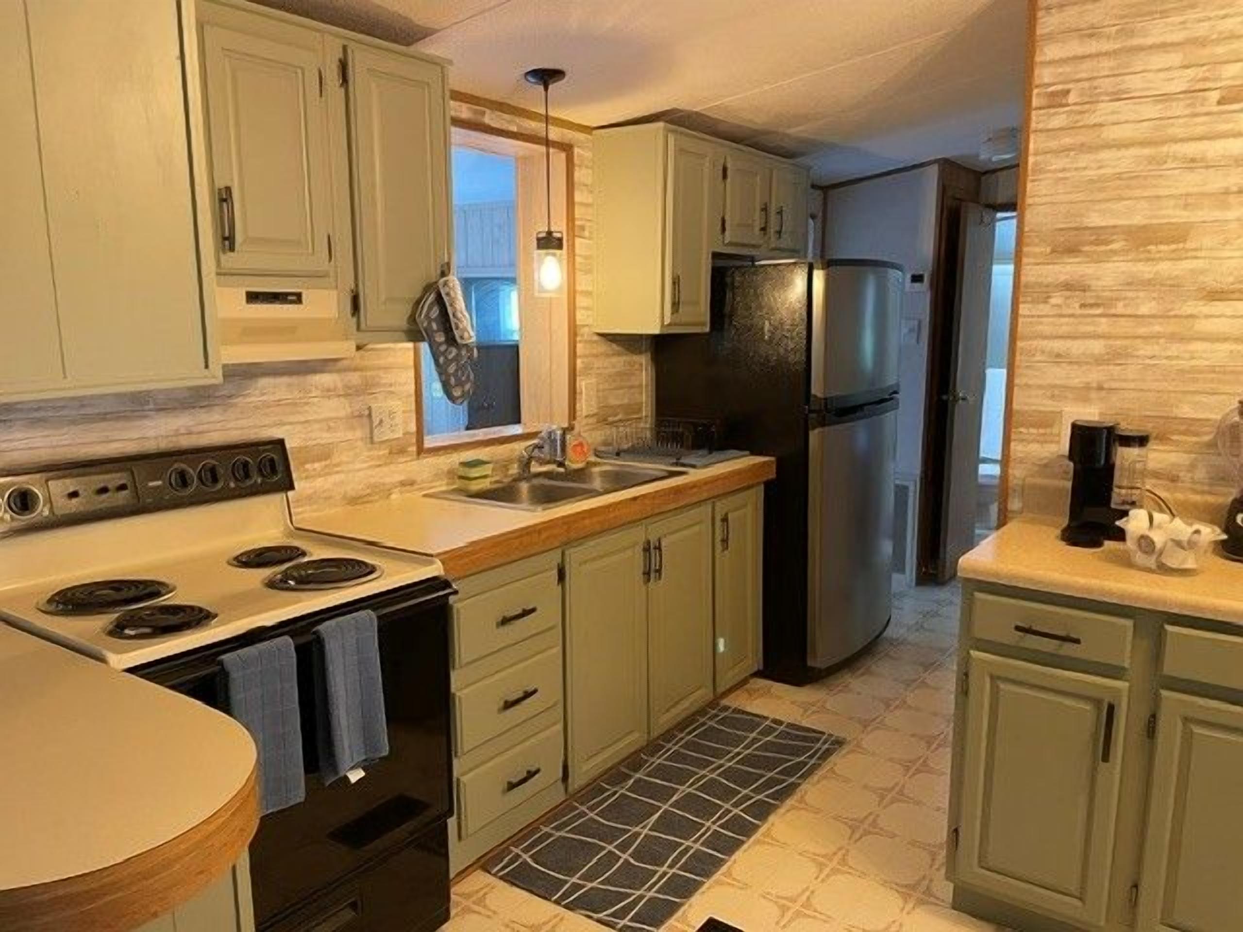 Una cocina con gabinetes verde claro, un refrigerador de acero inoxidable y salpicadero de azulejos.