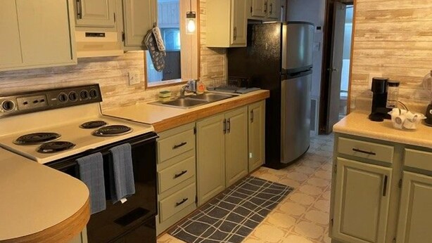 A kitchen with light green cabinets, a stainless steel refrigerator, and a tiled backsplash.