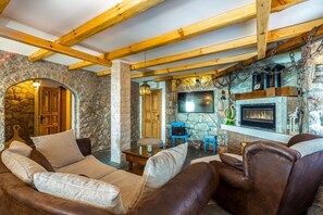 A cozy living room with stone walls, wooden beams, a fireplace, and comfortable seating. - Cozy 2-bedroom house in a serene spot with AC (Jablanac)