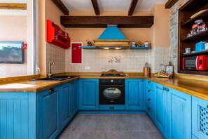 Een keuken met blauwe kastjes, een houten aanrecht, een rode magnetron en een fornuis.