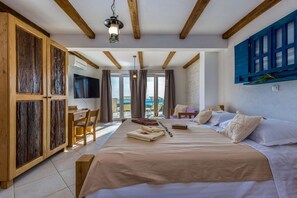 Ein Schlafzimmer mit einem großen Bett, Holzbalken, einem Fernseher und Blick ins Freie.