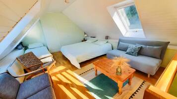 Et kompakt og moderne loftsværelse med skråvæg, seng, sofa, et lille bord og et vindue.