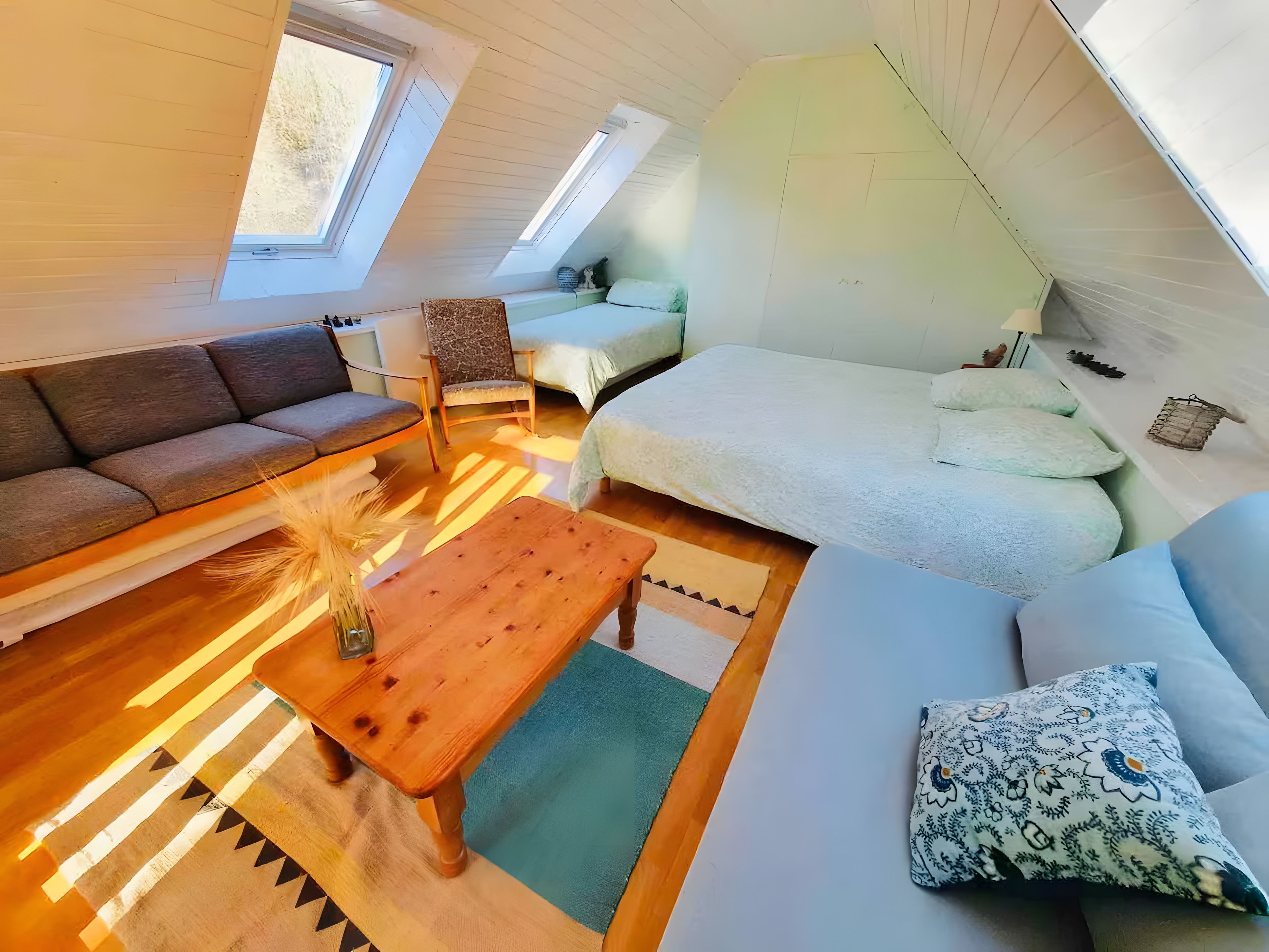 A cozy loft bedroom with a sofa, a chair, a bed, and a small table.