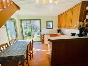 A kitchen with wooden cabinets, a dining table with chairs, and a view of the outdoors through a sliding glass door.
