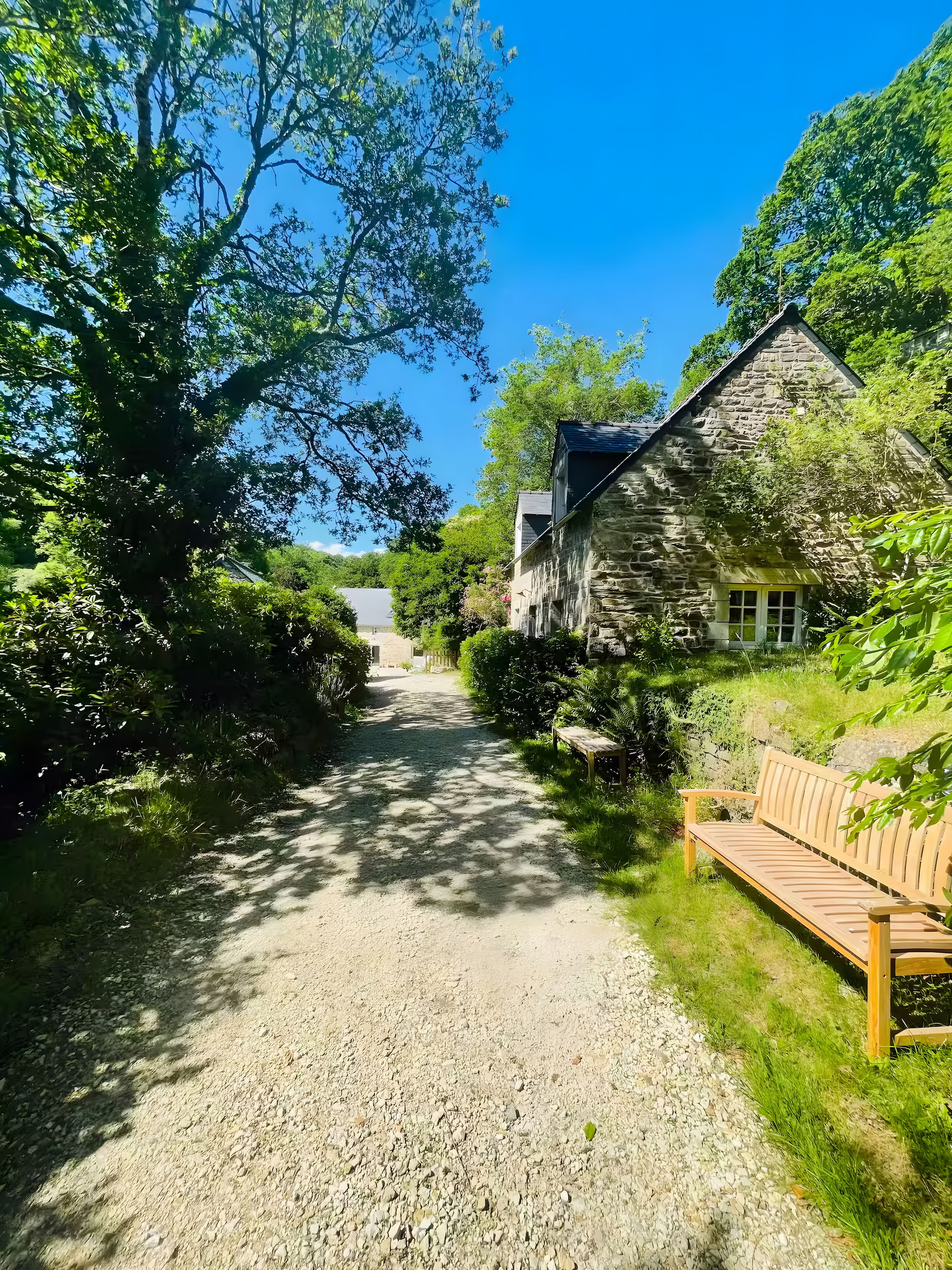 A gravel path leading to a stone building with a wooden bench on the right.