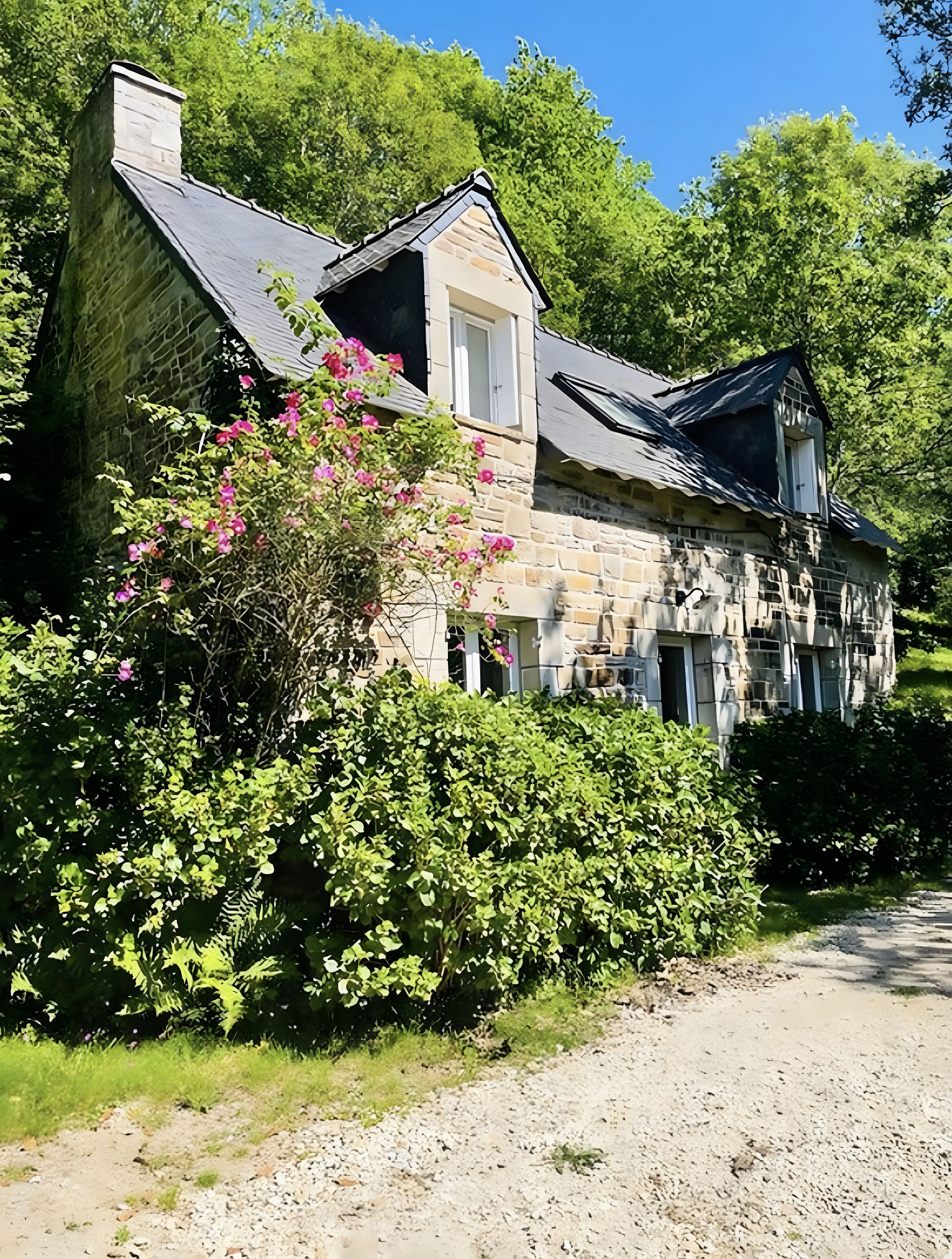 Een stenen huis met schuin dak, omgeven door weelderige begroeiing en een grindpad.