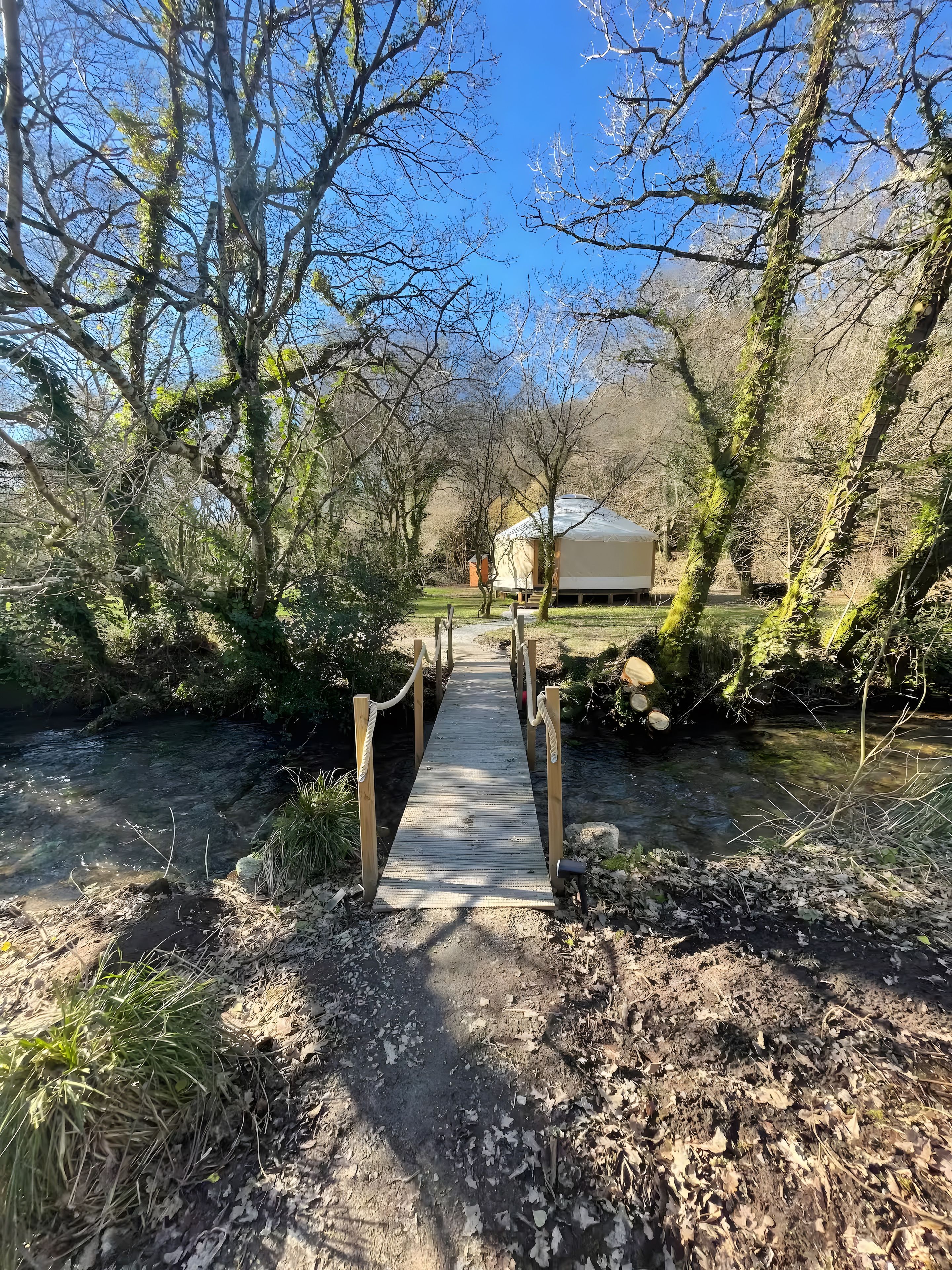 Un pont en bois menant à une yourte située dans une zone boisée.