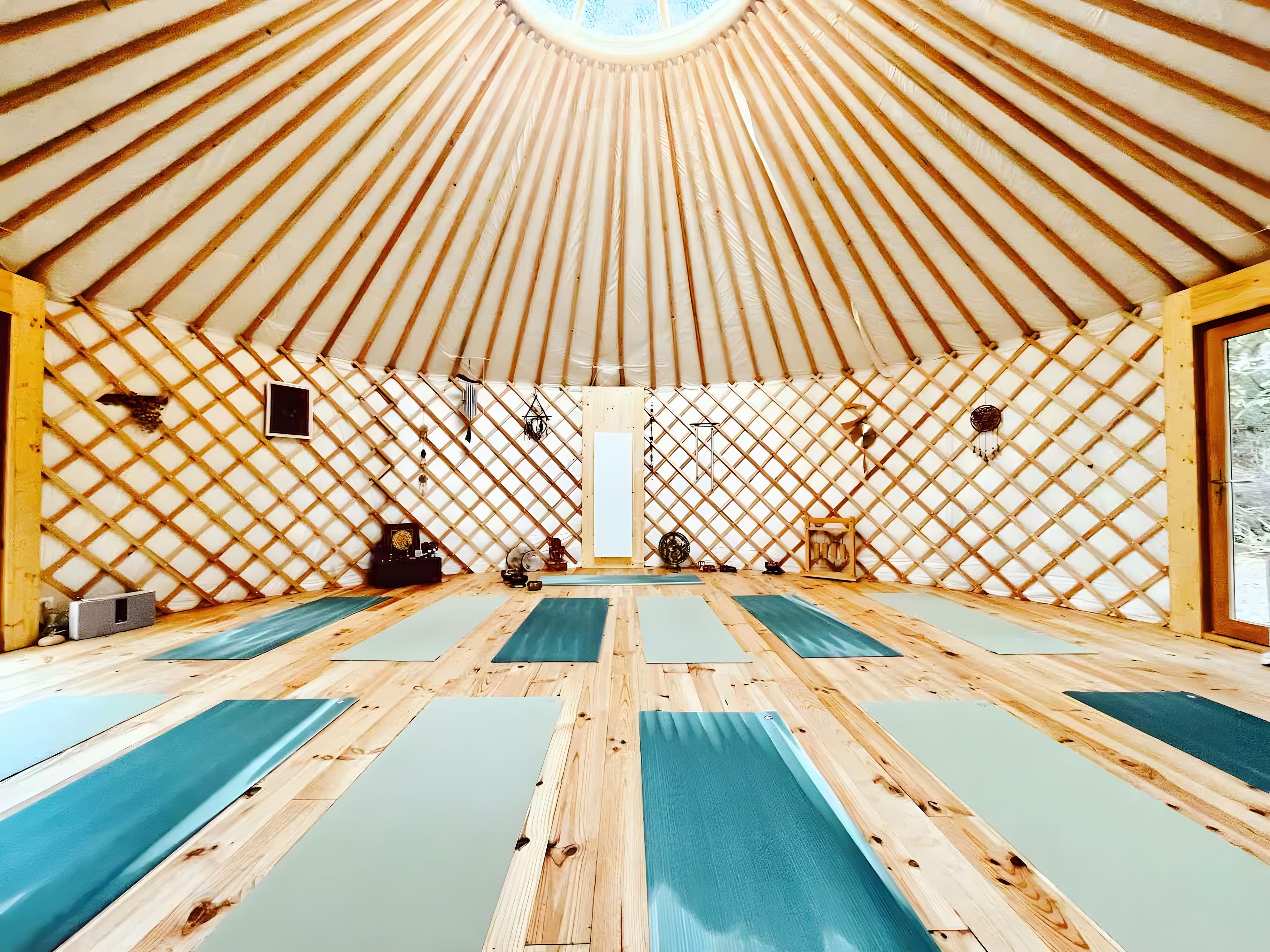 Une pièce spacieuse avec un plafond haut et un mur en treillis de bois. Plusieurs tapis de yoga sont alignés sur le sol.