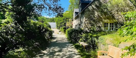 A gravel path leading to a stone building with a wooden bench on the right.