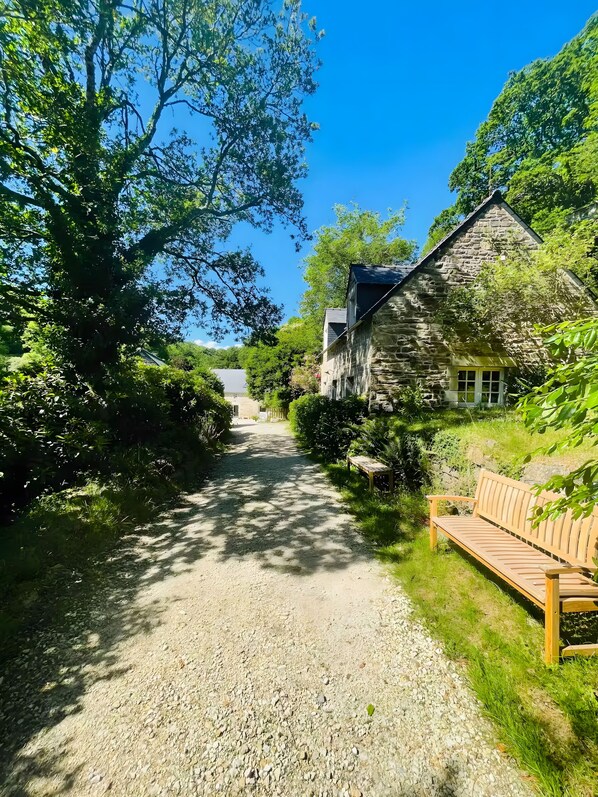 A gravel path leading to a stone building with a wooden bench on the right.