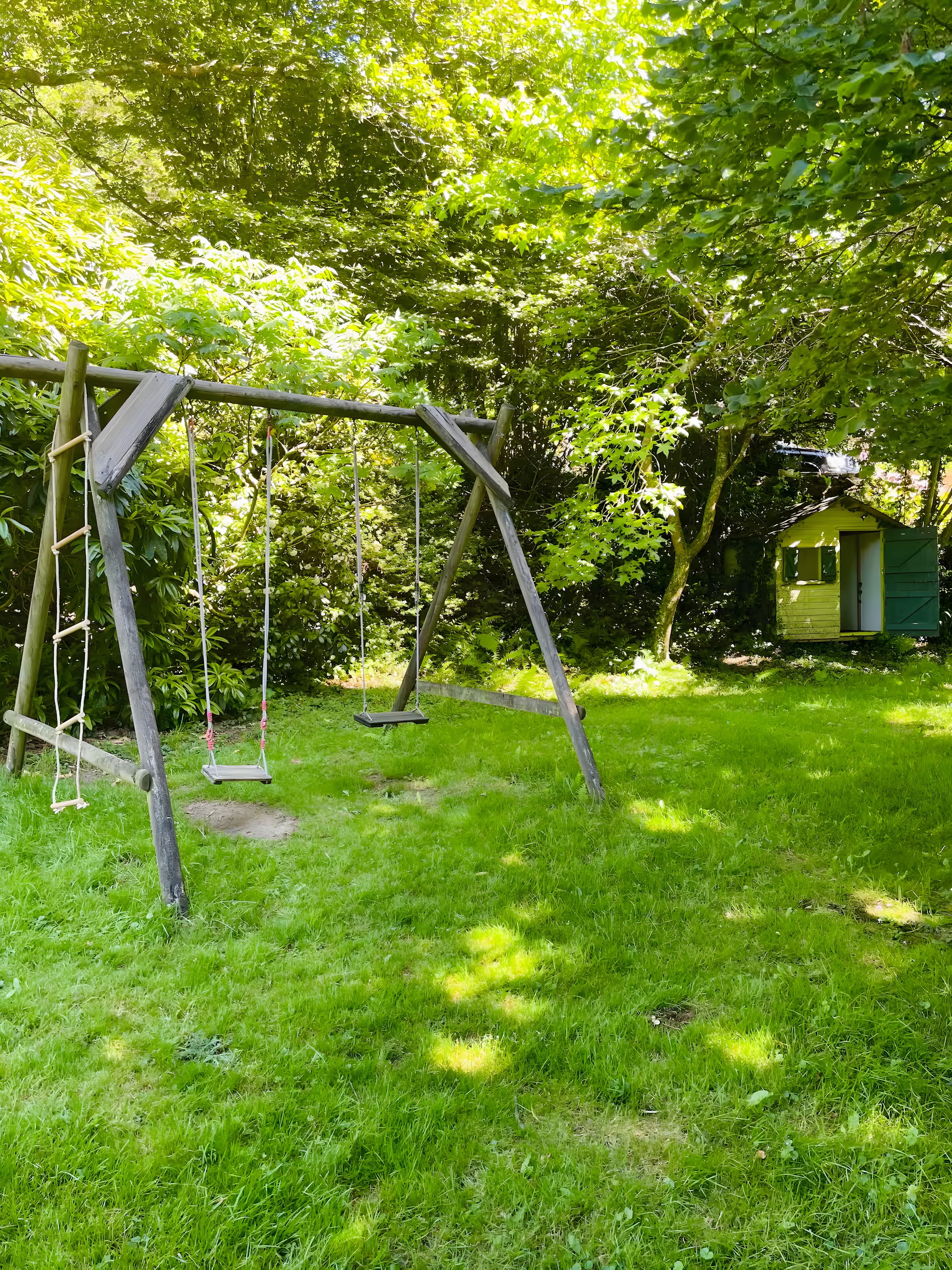 A wooden swing set in a grassy yard with a small shed in the background.