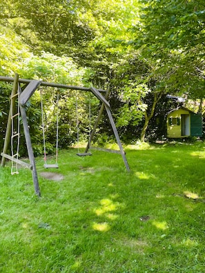 A wooden swing set in a grassy yard with a small shed in the background.