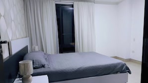 Une chambre à coucher moderne, avec un lit, une table de chevet et une fenêtre avec des rideaux.