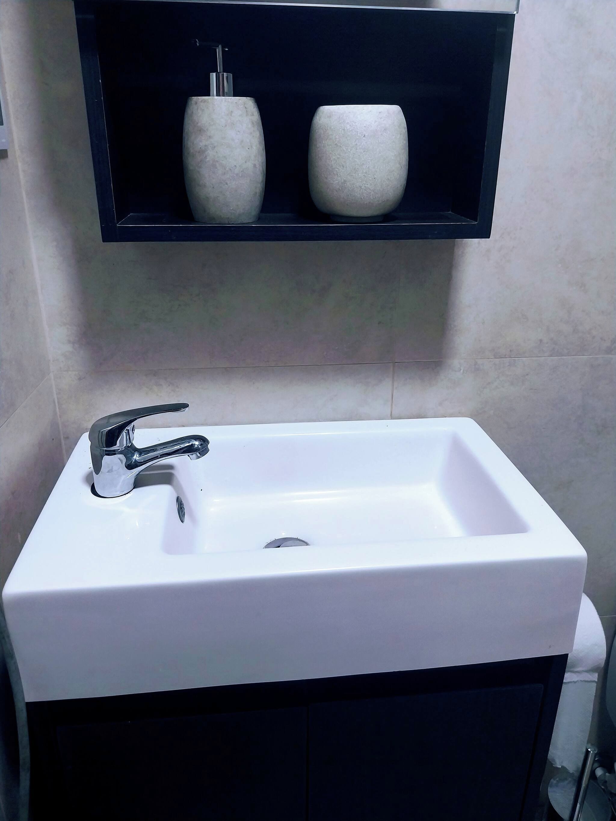 A bathroom with a white sink, chrome faucet, and a black cabinet below.