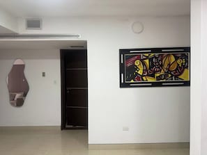 A room with a large abstract painting on the wall, a door, and a patterned object on the wall.