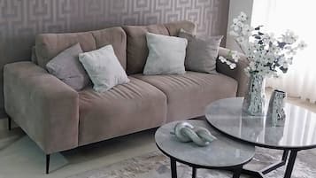 A modern living room with a beige sofa, two round glass tables, and a vase with white flowers.