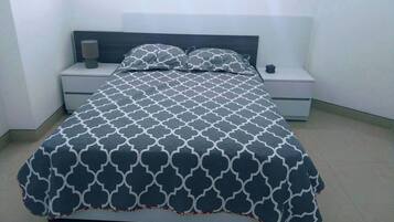 A bed with a patterned bedspread, two bedside tables, a lamp, and a nightstand.