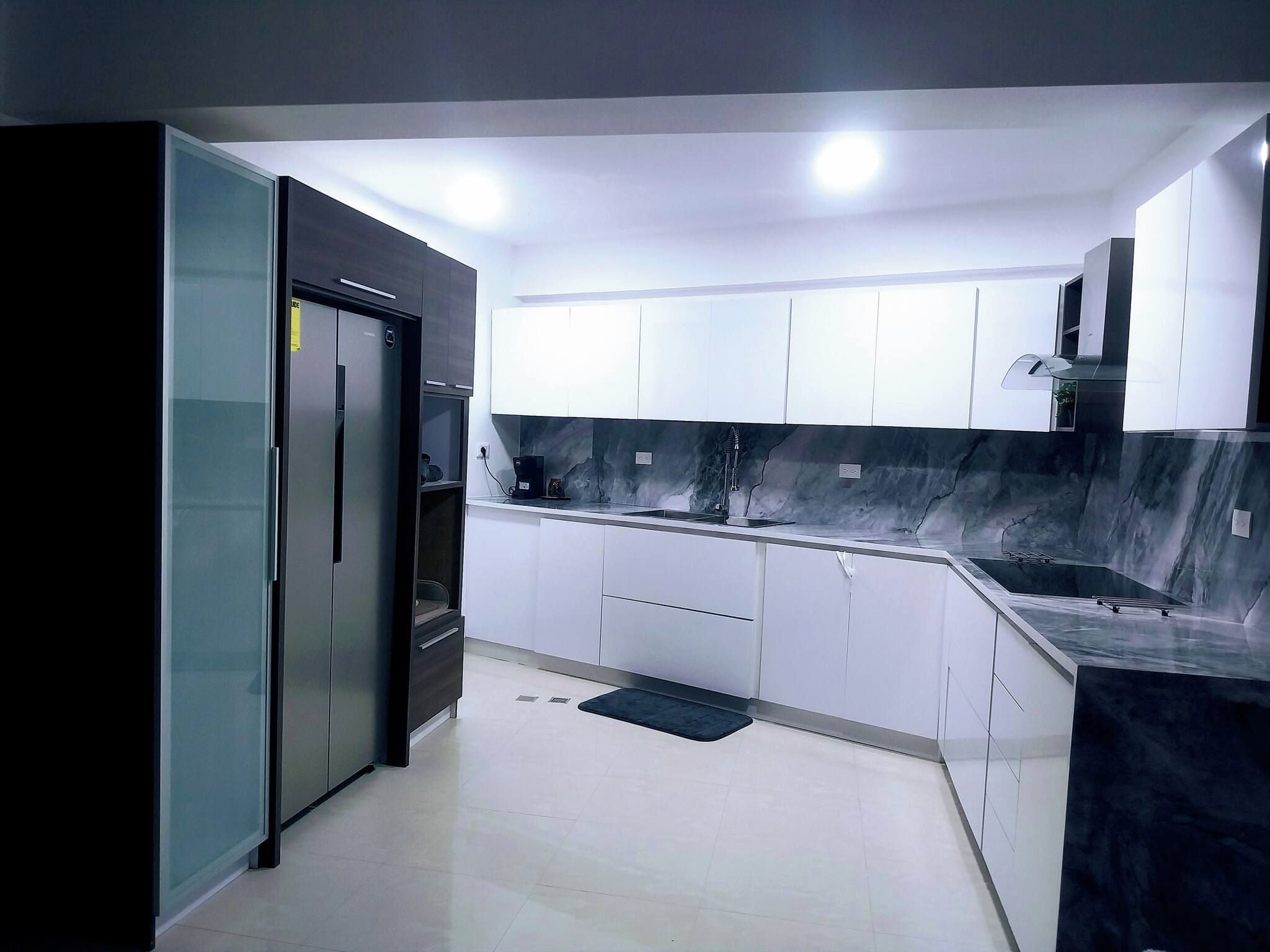 A modern kitchen with white cabinets, a black refrigerator, and a marble backsplash.