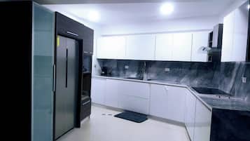 A modern kitchen with white cabinets, a black refrigerator, and a marble backsplash.