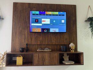 A television mounted on a wooden wall with a shelf below displaying decorative items. - Your Perfect Getaway in Margarita , 2 Bedrooms , Pool View (Aguirre)