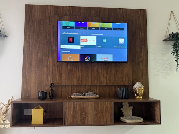 A television mounted on a wooden wall with a shelf below displaying decorative items.