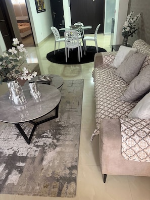 A living room with a sofa, a round table, and two chairs. There is a rug on the floor and a vase with flowers on a table.