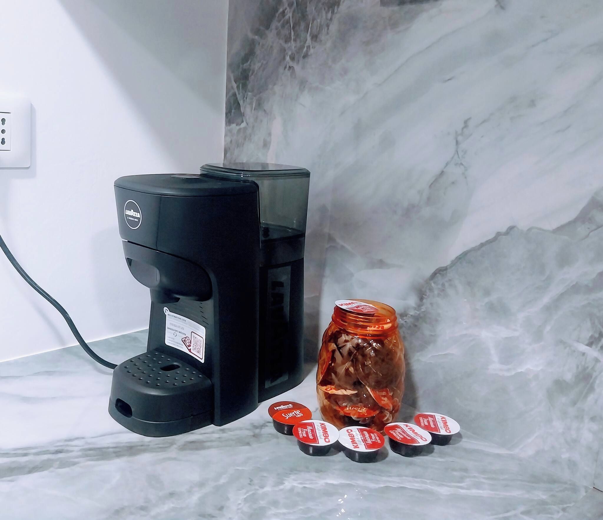 Een koffiezetapparaat, een pot met deksel, en verschillende kleine bakjes met etiket op een marmeren aanrecht.