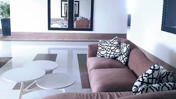 A modern living room with a brown sofa, two white round tables, and a large mirror with a black frame.