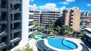 Un hôtel à plusieurs étages doté d’une piscine centrale, d’un espace extérieur aménagé et de palmiers.