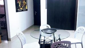 Un salon moderne avec une table en verre et des chaises blanches, un tapis noir et une porte dotée d’un cadre foncé.