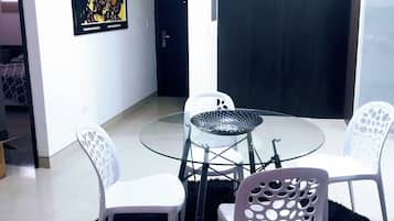 A modern living room with a glass table and white chairs, a black rug, and a door with a dark frame.